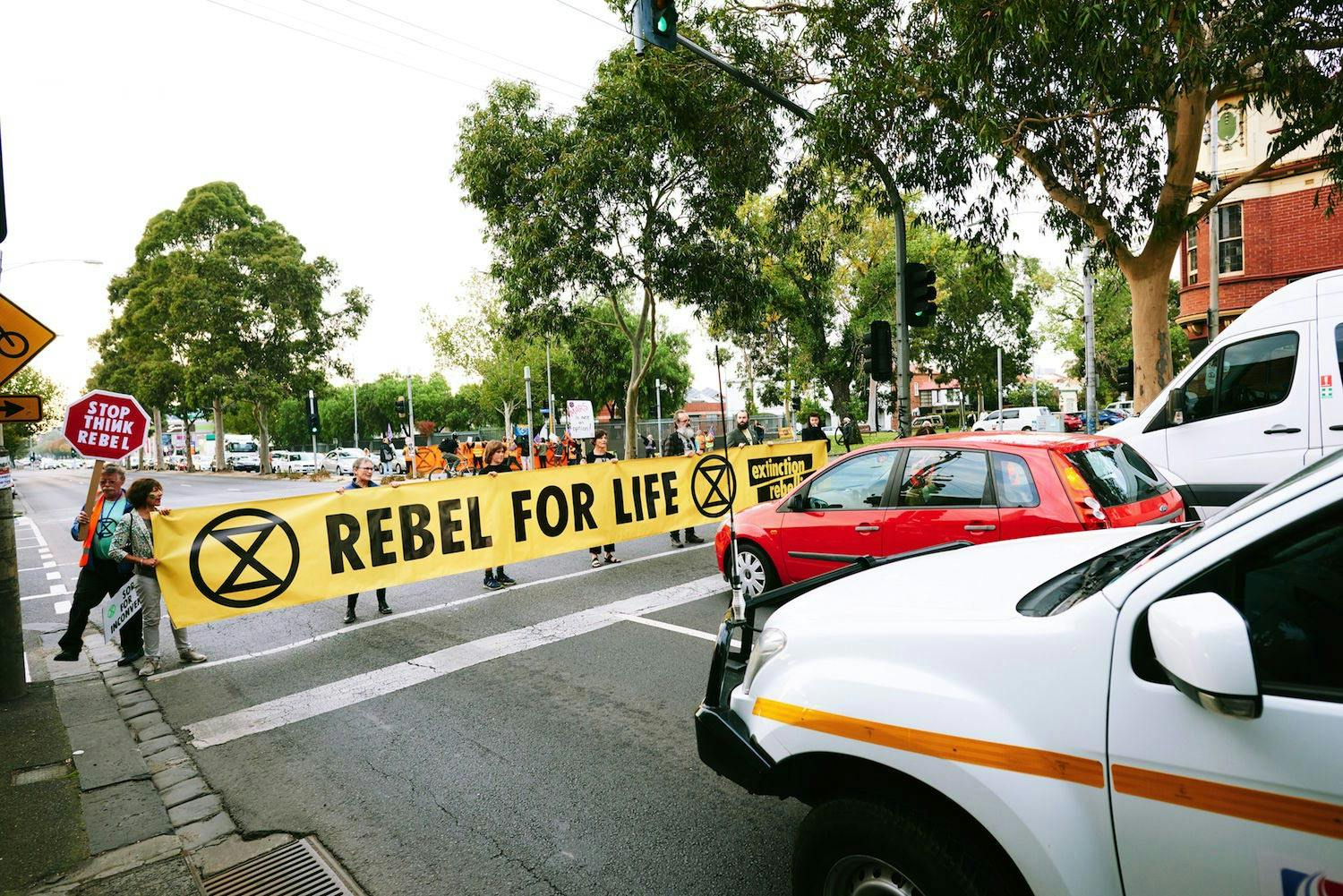 Photograph of activists holding a banner across the road, which reads: “Rebel for life”.