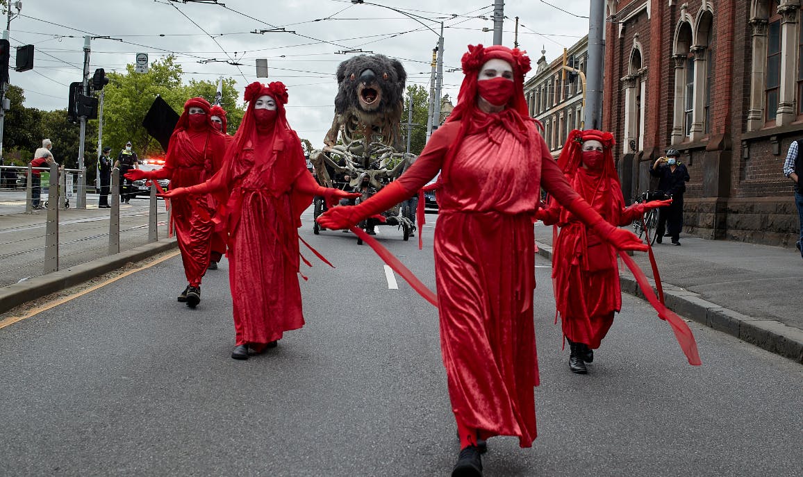 Extinction Rebellion Red Rebels march in sombre red dress followed by giant, burning, animated koala