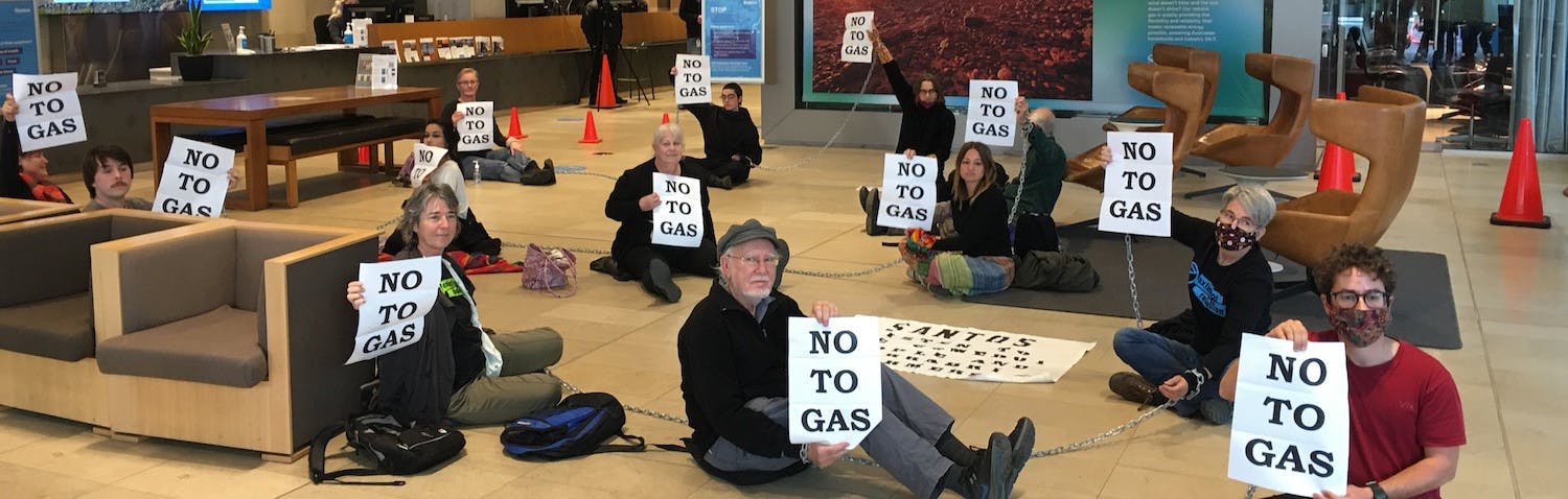 Rebels sitting on the floor holding 'No to gas' signs. 