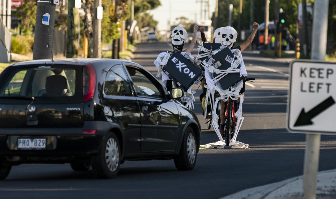 Black Car stops for Pelaton Skeleton bikes clutching briefcases reading Exxon blocking the road