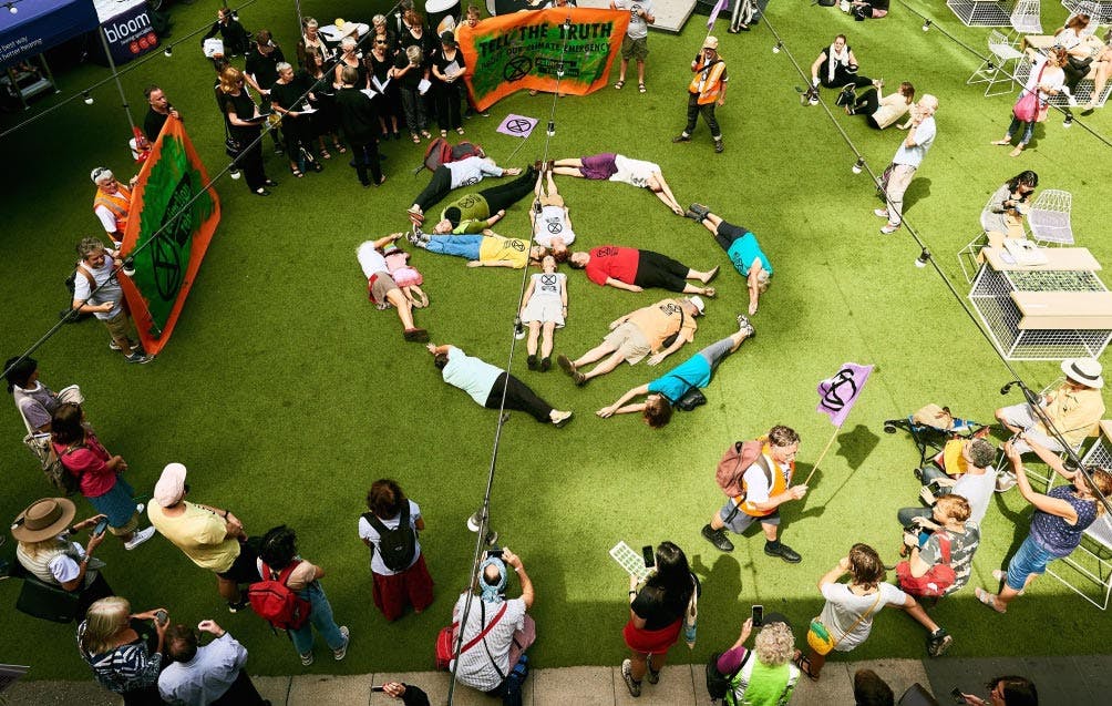 Photograph of activists participating in a die-in at QV shopping center, where they’re lying down in the shape of the extinction symbol