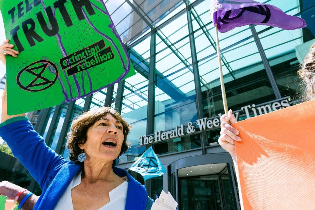 Photograph of a woman holding up a “Tell The Truth” placard, in front of the Herald Sun offices