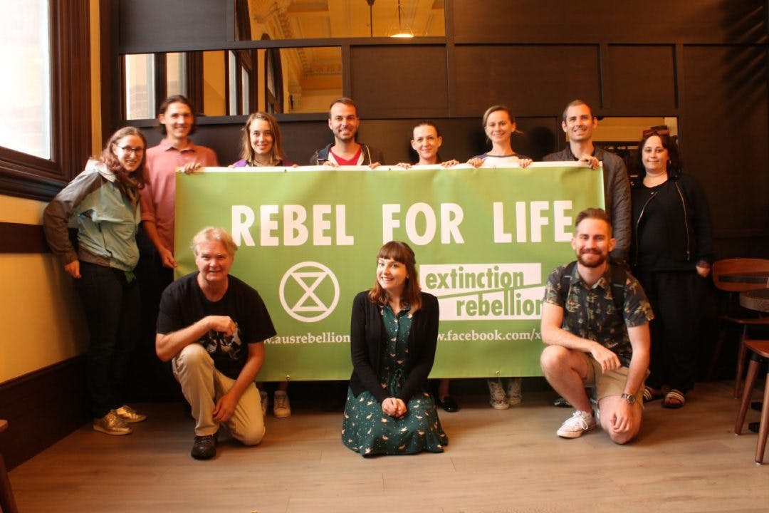 Photograph of XR NSW activists posing for a photograph in front of a banner that reads: “Rebel for life”