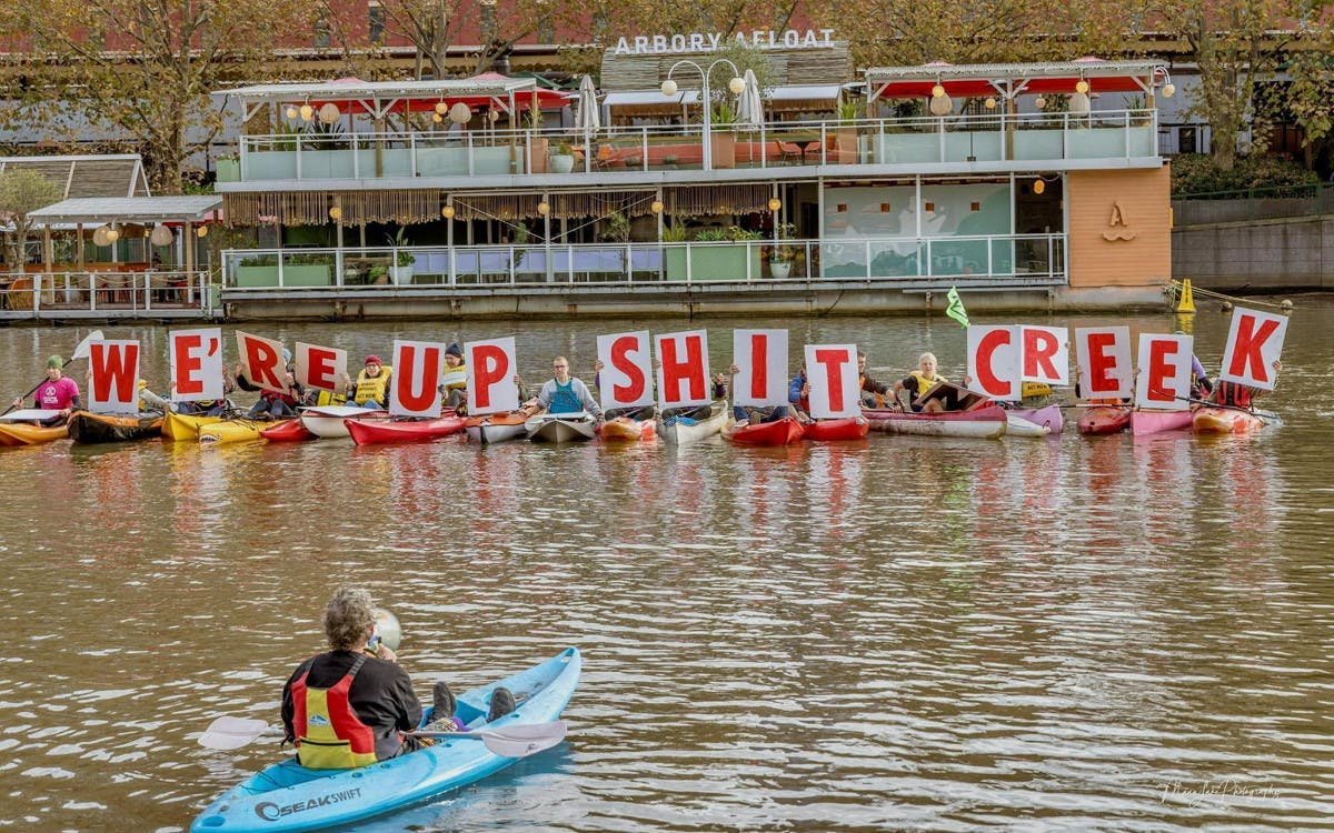 Canoe Flotillaholds signs reading 'We're up shit creek'