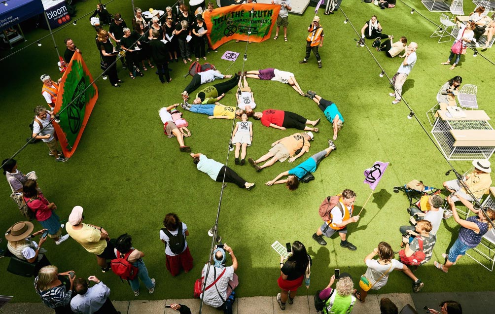 Photograph of activists participating in a die-in at QV shopping center, where they’re lying down in the shape of the extinction symbol